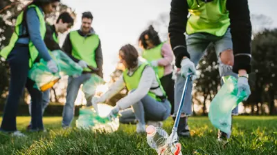A group of volunteers wearing vests and picking up litter at a park.