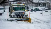 A snow plow going down a street pushing snow with its blade