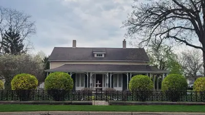 Outside exterior of a designated heritage home in Niagara Falls, showing decorative iron fencing, water fountain and green landscaping.