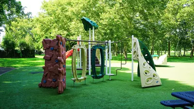 Playground equipment at Solar Park in Niagara Falls. Showing the green artificial turf surface and trees in the background.