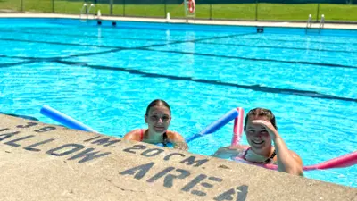 Children with pool tubes, enjoying an outdoor municipal pool on a sunny day.