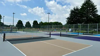 The outdoor pickleball courts at MF Ker Park in Niagara Falls with nets, people playing and a blue sky overhead.