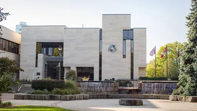 Front exterior entrance of City Hall in Niagara Falls Ontario on a sunny day, showing three flag poles and exterior landscaping.