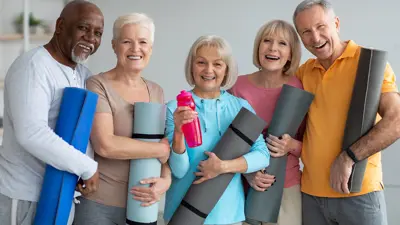 A group of five seniors smiling and holding their exercise mats.