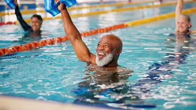 People smiling and exercising in the lanes of an indoor swimming pool. 
