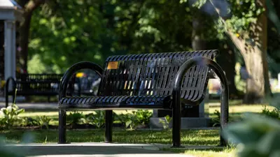 Black iron bench along a winding path with trees in background